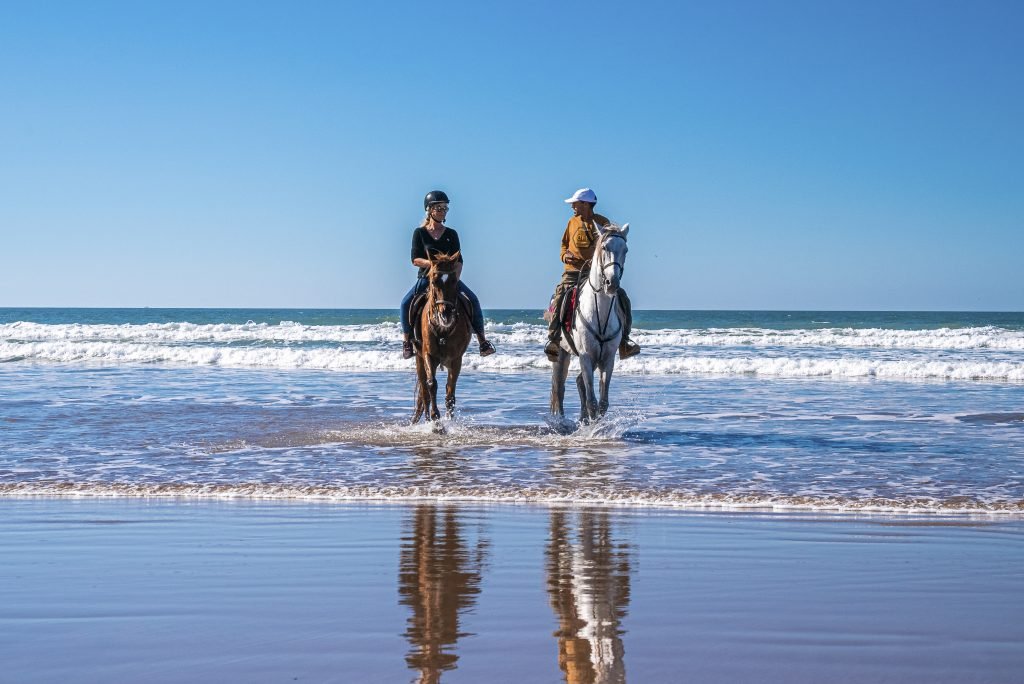 Man and woman riding horses along shoreline at beach against clear sky